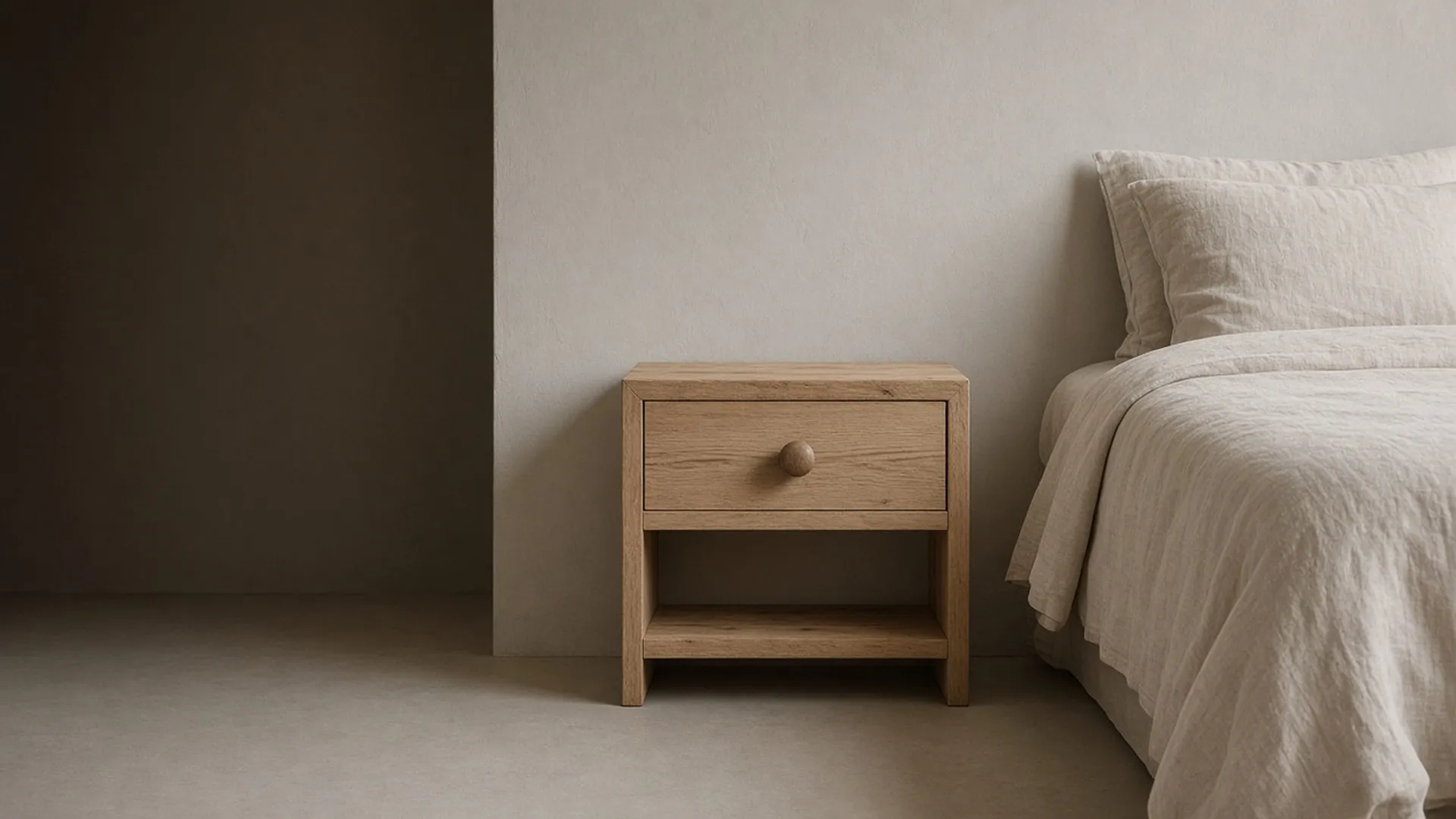 A bare unfinished wood nightstand with a closed drawer in a calm bedroom corner