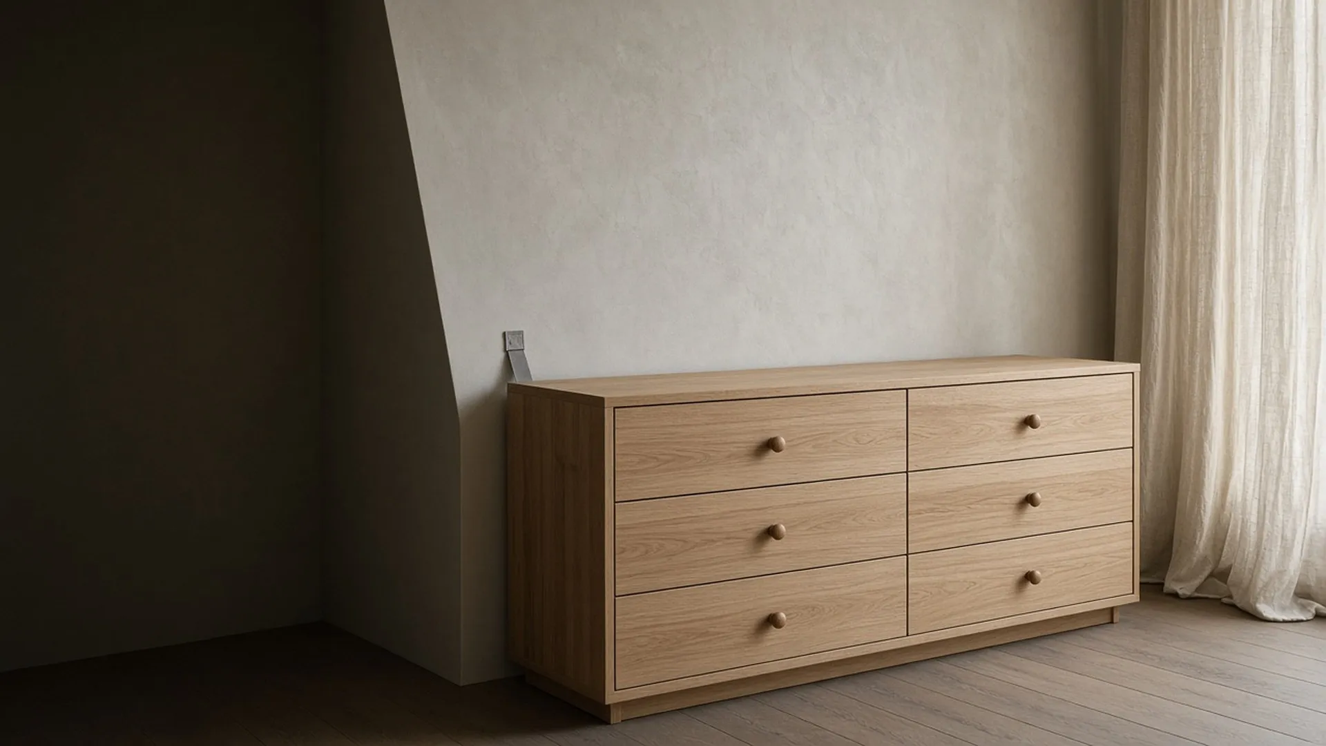 A bare wood dresser, drawers closed, against a wall with a small strap at back