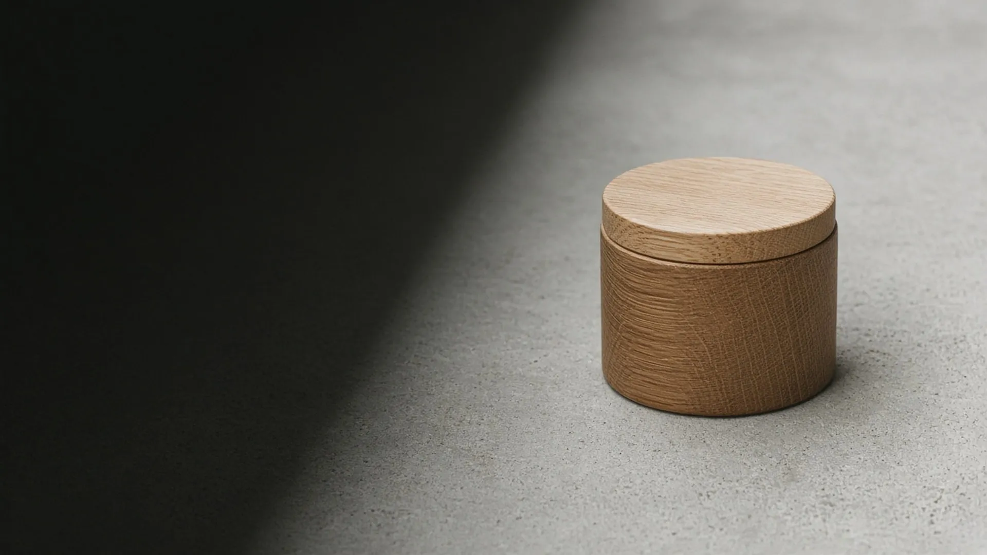 A closed round wooden container with a fitted lid on bare concrete