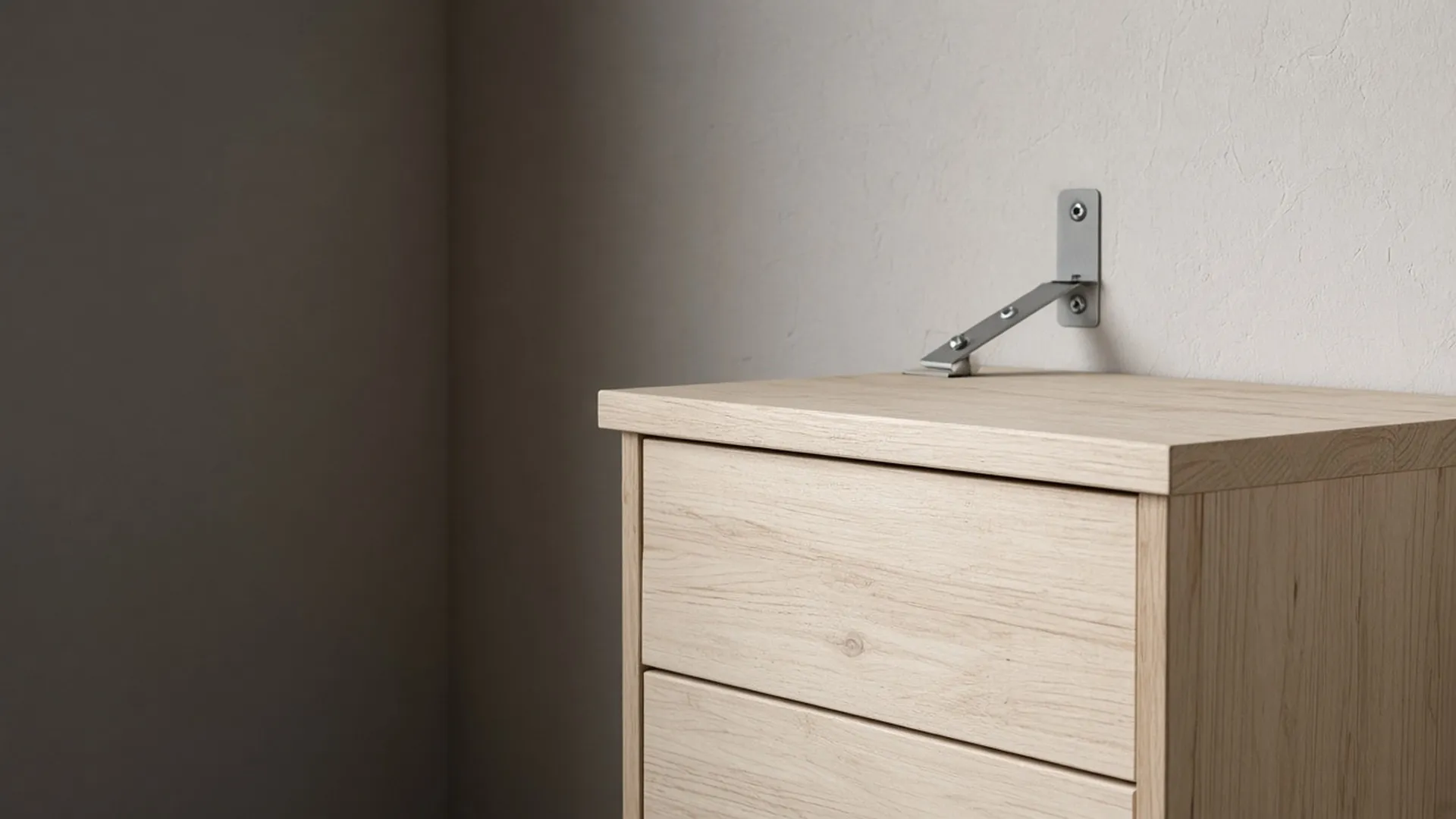 A plain metal bracket and strap joining the back of a dresser to a wall