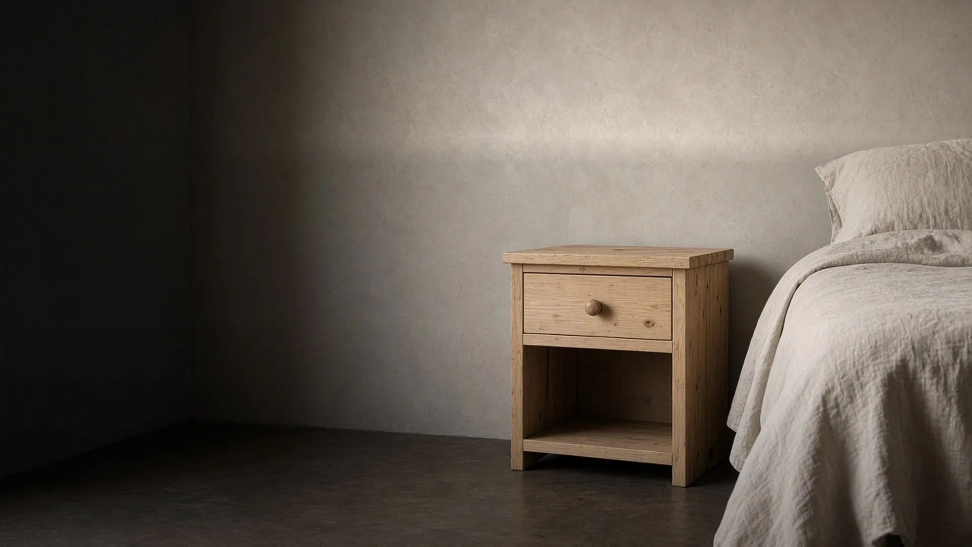 A bare unfinished wood nightstand with a closed drawer in a calm bedroom corner